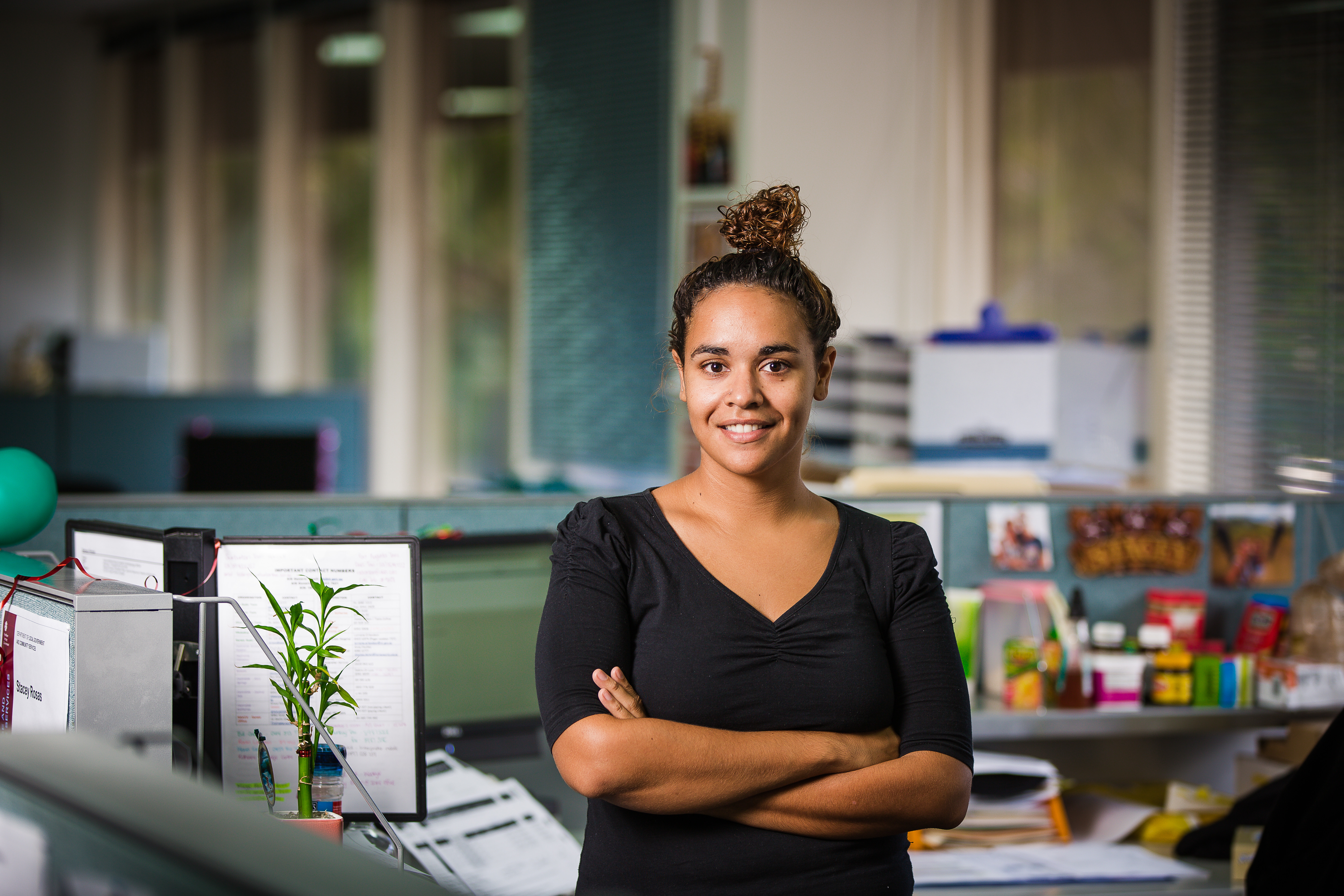  A woman in a black top is smiling with arms crossed in an office